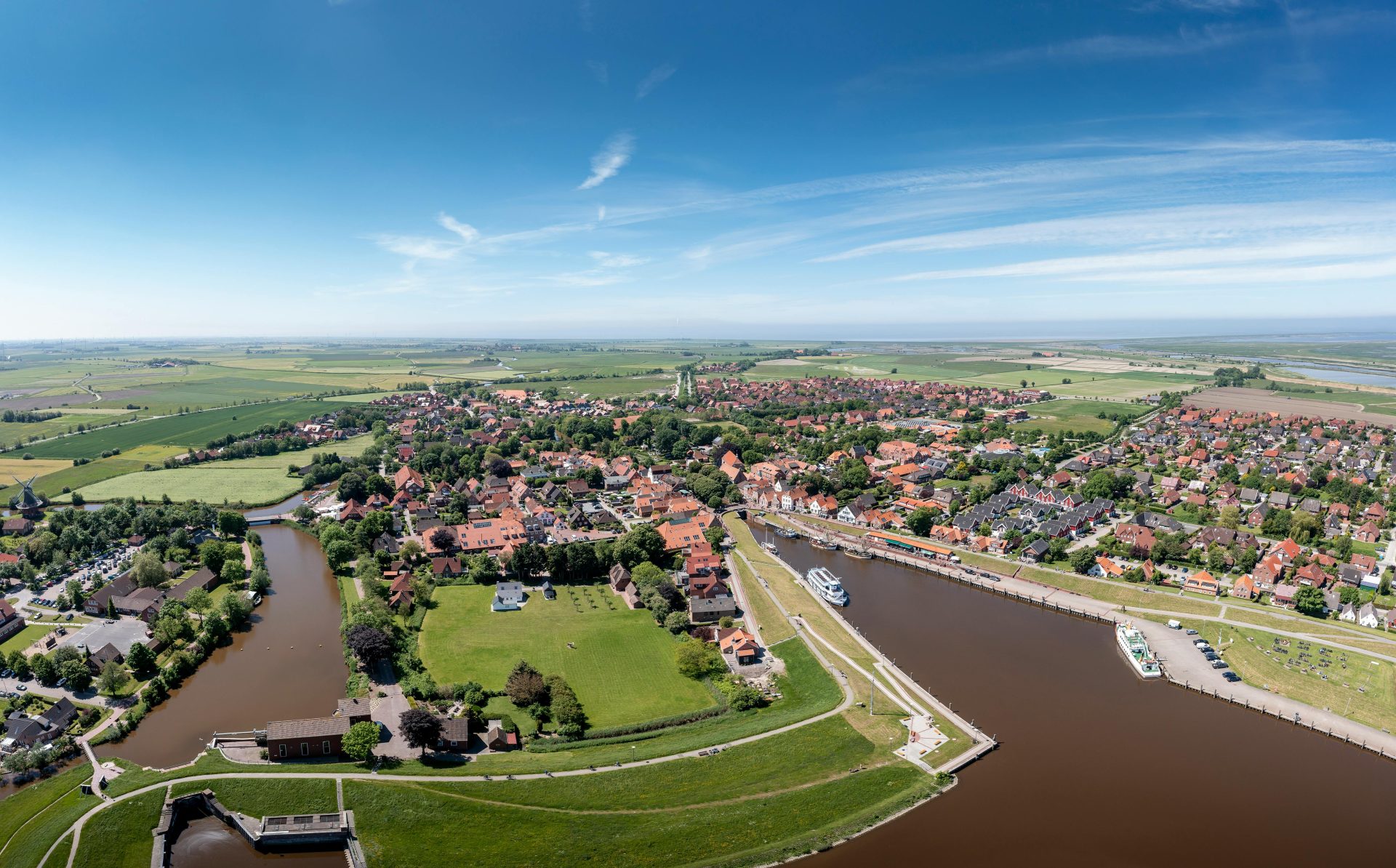 A scenic aerial view of Krummhörn, Germany with fields, river, and clear sky.